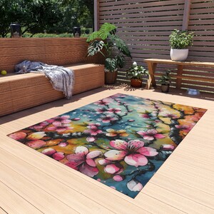 May include: A colorful area rug with a watercolor painting of pink cherry blossoms on a blue and green background.