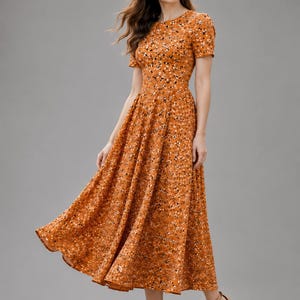 May include: A midi-length dress in a burnt orange hue featuring a dense, speckled pattern of small white and black dots. The garment has a round neckline, short sleeves, and a fitted bodice that transitions into a full, flared skirt.