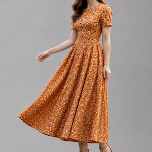 May include: A midi-length dress in a warm mustard-orange hue featuring a dense, small-scale floral pattern in black and white. The garment has a round neckline, short sleeves, a fitted bodice, and a full, pleated skirt that flares at the waist.