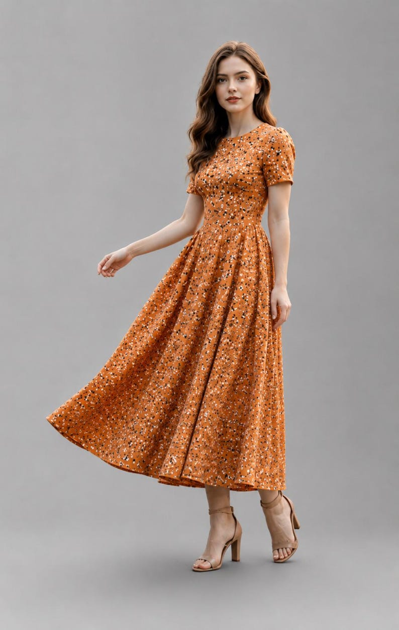 May include: A midi-length dress in a warm mustard-orange hue featuring a dense, small-scale floral pattern in black and white. The garment has a round neckline, short sleeves, a fitted bodice, and a full, pleated skirt that flares at the waist.