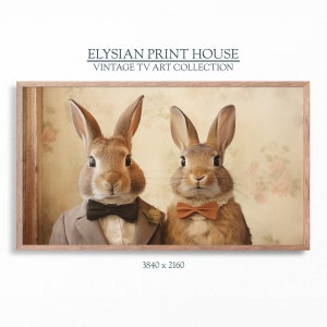 May include: Two brown rabbits wearing bow ties and formal attire. The rabbits are looking directly at the camera. The background is a light brown with a floral pattern. The image is titled "Elysian Print House Vintage TV Art Collection".