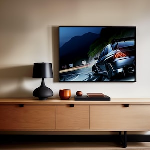 May include: A modern living room setup featuring a large flat-screen TV displaying a car racing scene. A black lamp, a small orange pot, and a wooden tray with a book are on a wooden cabinet. The cabinet has black handles and legs.