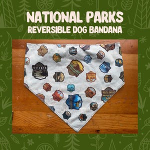 May include: Reversible dog bandana with a light blue background and various National Park patches. The bandana features patches for Glacier, Yosemite, Arches, and Rocky Mountain National Parks. The text "NATIONAL PARKS REVERSIBLE DOG BANDANA" is at the top.