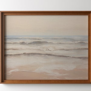 May include: A framed painting of a seascape with soft, muted colors. The painting depicts a calm ocean with gentle waves and a sandy beach in the foreground. The sky is a pale blue, and the water is a light blue-gray. The painting is framed in a simple wooden frame.
