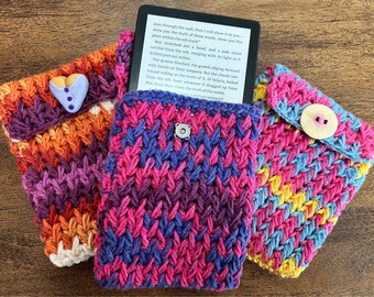 May include: Three crocheted e-reader covers in different color combinations. The covers are made with a chevron stitch pattern. The covers are in shades of pink, purple, blue, yellow, orange, and white.