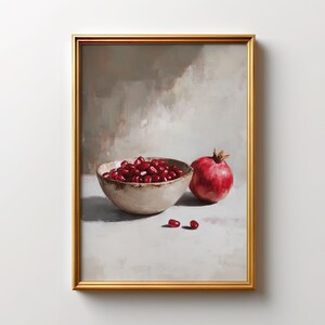 Puede incluir: Una lámina de arte enmarcada con una pintura al óleo de un cuenco de cerámica beige lleno de semillas de granada de color rojo intenso, acompañada de una granada entera y dos semillas sueltas sobre un fondo neutro y difuminado.