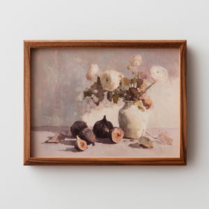 Puede incluir: Pintura enmarcada de naturaleza muerta con un jarrón blanco lleno de flores blancas y follaje. Varias higos, algunos cortados por la mitad, están dispuestos frente al jarrón. La obra de arte tiene una paleta de colores suaves y un marco de madera.
