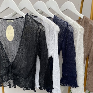 May include: Five sheer knit cardigans in black, white, navy blue, cream, and brown hanging on hangers. The black cardigan has a label that says "ikat".