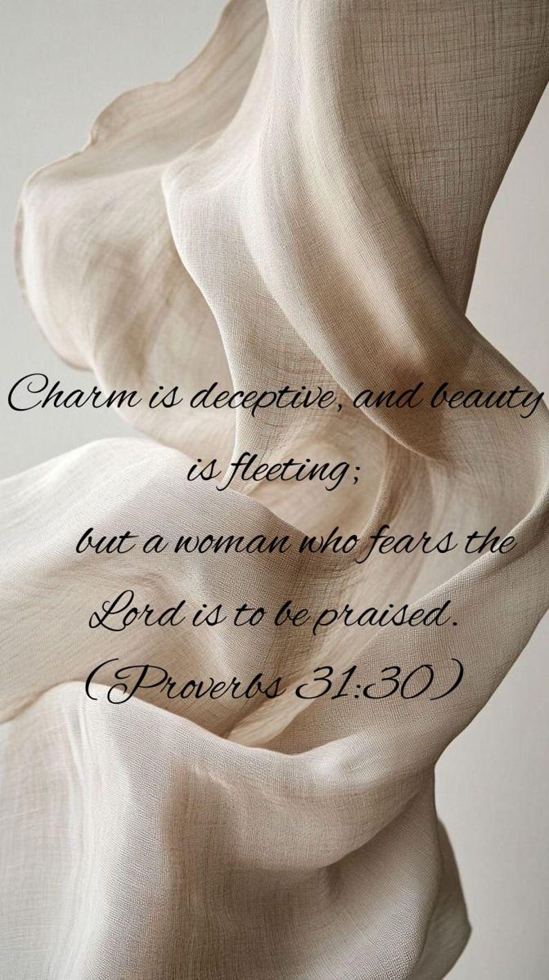May include: A beige fabric with the text "Charm is deceptive, and beauty is fleeting; but a woman who fears the Lord is to be praised. (Proverbs 31:30)". The fabric is draped and has a textured appearance.