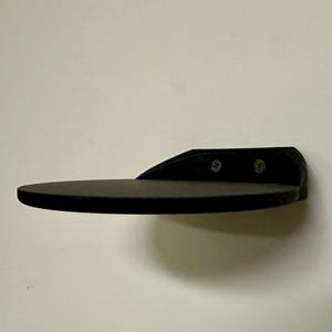 May include: A black wall-mounted shelf with a rounded edge. The shelf is made of a smooth, hard material and has two visible screws.