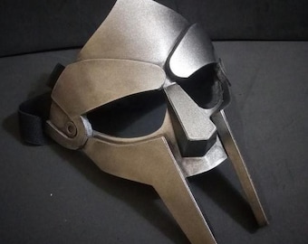 May include: A silver and brown plastic mask with a raised design. The mask has a strap that goes around the head.