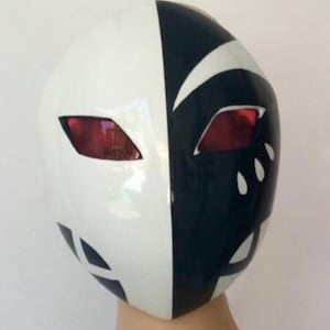 Puede incluir: Una máscara de dos tonos, dividida verticalmente con un diseño blanco y negro. La máscara presenta aberturas rojas para los ojos y detalles blancos. La máscara es probablemente para disfraces o cosplay.