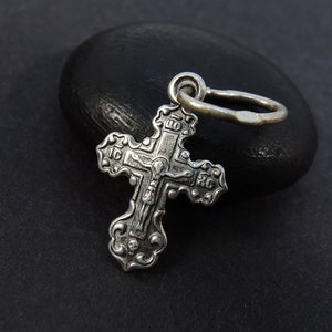 Peut inclure: Un pendentif en argent en forme de croix avec des détails complexes et une figure de Jésus-Christ sur le devant. La croix a une boucle en haut pour l'attacher à une chaîne.
