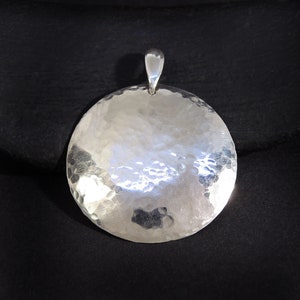 May include: A silver pendant with a hammered, circular design. The pendant has a simple bail for attaching to a chain.