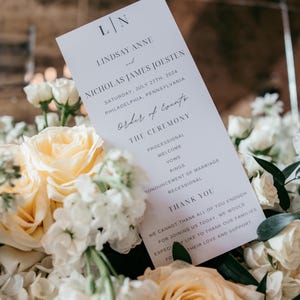 Pode incluir: Um programa de casamento com os nomes de Lindsay Anne e Nicholas James Joesten, e a data de 27 de julho de 2024. O programa &eacute; rodeado por rosas brancas e p&ecirc;ssego e outras flores brancas.