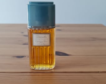 May include: A clear glass bottle of Diorissima Eau de Toilette perfume by Christian Dior. The bottle has a blue cap and a gold label with the name of the perfume.