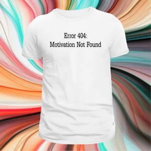 May include: A white short-sleeved t-shirt featuring the black printed text Error 404: Motivation Not Found centred on the chest. The garment has a classic crew neckline and a standard fit, presented against a colourful, swirling abstract background.