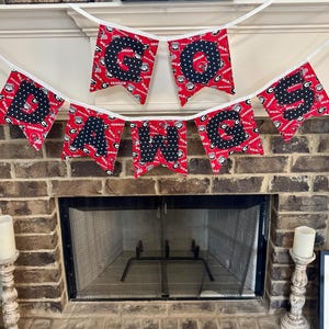 May include: A red and black fabric banner spelling out "GO DAWGS" is strung across a fireplace. Each pennant features a letter in black polka dots on a red background with "GEORGIA" text. The banner is suspended above a brick fireplace.