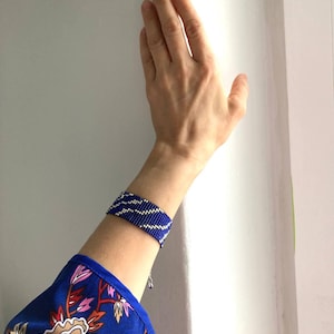 May include: A blue and silver beaded bracelet with a wavy pattern. The bracelet is worn on a person's wrist.