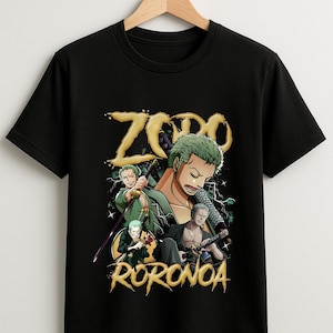 May include: Black t-shirt featuring a graphic of a character with green hair and swords. The design includes the word "Zoro" in gold lettering at the top and "Roronoa" at the bottom. The character is depicted in multiple poses.