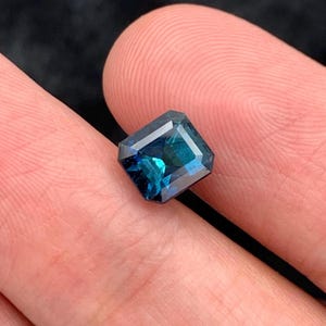 May include: A deep blue emerald cut gemstone with a slight green hue.