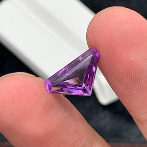 May include: A deep purple amethyst gemstone with a triangular cut and a faceted finish.