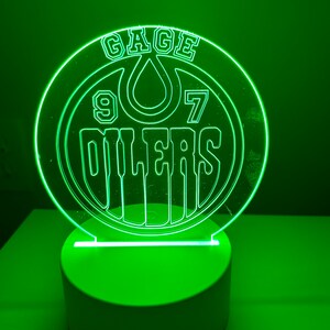 May include: Green LED night light with a clear acrylic base featuring a white outline of the Edmonton Oilers logo with the text "Gage 97 Oilers".