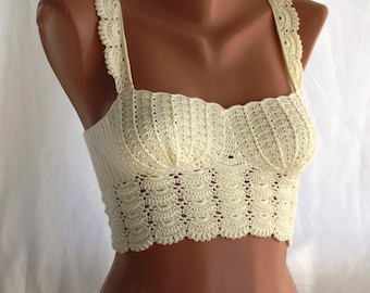 May include: A crocheted crop top in a cream color with a scalloped edge. The top has thin straps and a square neckline.