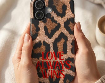 Könnte beinhalten: Eine Smartphone-Hülle mit braun-schwarzem Leopardenmuster. Der Text LOVE ALWAYS WINS ist in roten Großbuchstaben im unteren mittleren Bereich der Hülle aufgedruckt. Die Hülle verfügt über eine Aussparung für eine Doppelkamera.
