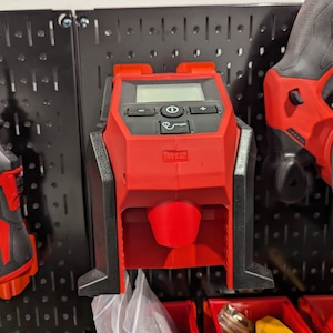 Peut inclure: Un outil électrique Milwaukee rouge et noir avec un écran numérique et une poignée noire. L'outil est monté sur un panneau perforé.