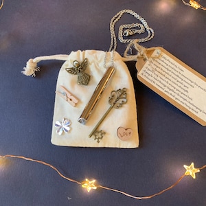 May include: A small white pouch containing a silver necklace, a key, a wooden heart with the word "Love" on it, and a small tag with the text "This little pocket of Calm is to encourage the practice of deep mindful breathing exercises. An angel to protect and guide you. A charm to unlock your inner strength. A penny to check your luck. A pair of clothes pegs to bring you good luck. A heart to hold things together through challenging times. And a heart to remind you that you are truly loved."