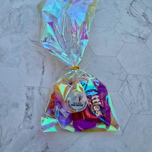Puede incluir: Una bolsa de pl&aacute;stico transparente e iridiscente llena de caramelos surtidos. La bolsa est&aacute; atada con una banda el&aacute;stica amarilla. Una pegatina redonda blanca con texto negro dice "You've Been Pixie Dusted! The Smith Family - Staten Island".