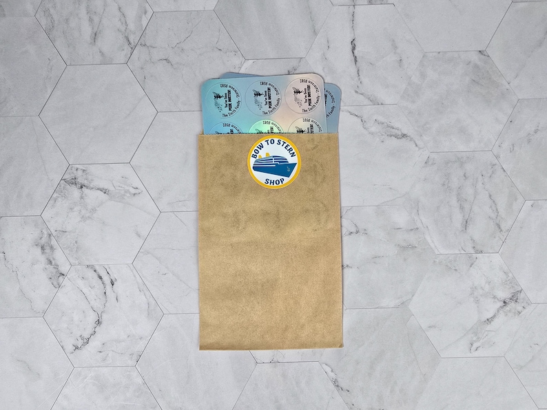 Puede incluir: Un sobre de papel marr&oacute;n con una pegatina que dice "Bow to Stern Shop" y una ilustraci&oacute;n azul y blanca de un crucero. El sobre contiene una pila de pegatinas blancas con dise&ntilde;os azules y blancos.