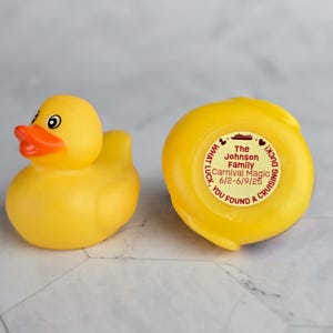 May include: A yellow rubber duck with a red beak and eyes. The duck has a sticker on the bottom that says "The Johnson Family Carnival Magic 6/2-6/9/25 YOU FOUND A CRUISING DUCK! WHAT LUCK."