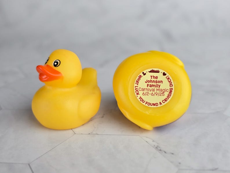 May include: A yellow rubber duck with a red beak and eyes. The duck has a sticker on the bottom that says "The Johnson Family Carnival Magic 6/2-6/9/25 YOU FOUND A CRUISING DUCK! WHAT LUCK."