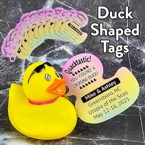 May include: A yellow rubber duck with sunglasses and a pink ribbon around its neck. A rainbow duck-shaped tag with the text "Quacktastic! You found a cruising duck!" and "Mike & Ashley Greensboro, NC Utopia of the Seas May 12-16, 2025" is attached to the duck.