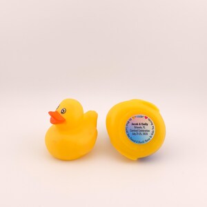 May include: Two yellow rubber duck toys. One duck is upright, with an orange beak and black eyes. The other duck is on its side, with a sticker that reads "Jacob & Emily Orlando, FL Carnival Celebration July 21-25, 2023".