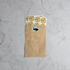 May include: A brown paper envelope with a white sticker that says "Bow to Stern Shop" and a black silhouette of a ship. The envelope is filled with white round stickers with red and yellow designs.