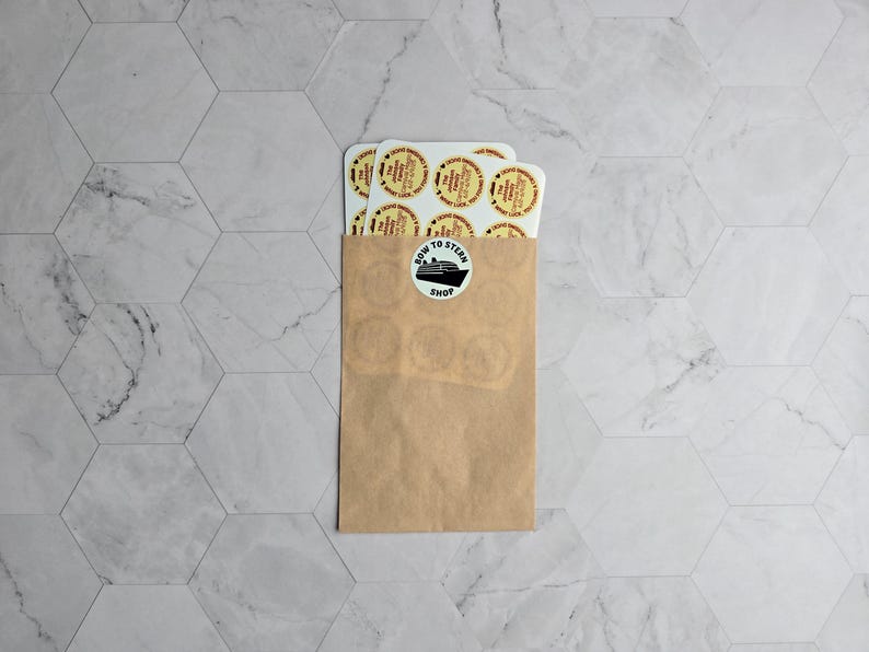May include: A brown paper envelope with a white sticker that says "Bow to Stern Shop" and a black silhouette of a ship. The envelope is filled with white round stickers with red and yellow designs.