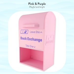 May include: A pink and purple Duck Exchange box with the text "Duck Exchange" and instructions to "Leave One" and "Take One." The box has a mailbox-like design with a top compartment and a lower open shelf. The text "Pink & Purple" and "Playful and bright" are at the top.