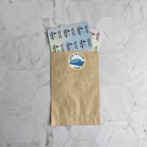 May include: A brown paper bag with a sticker that says "Bow to Stern Shop" and a blue and white illustration of a boat. The bag is filled with a stack of colorful tickets.