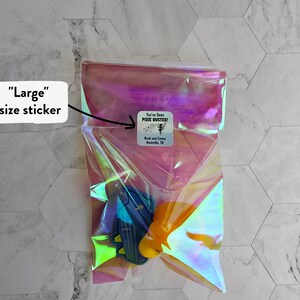 May include: A clear iridescent plastic bag with a sticker that says "You've Been Pixie Dusted!"  The bag contains a blue and yellow toy. The sticker also says "Ruth and Emma Nashville, TN".