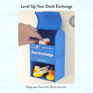 May include: A blue Duck Exchange box with the text "Duck Exchange" and "Leave One" and "Take One". The box contains rubber ducks, including a white duck and a yellow duck wearing a sailor hat. The text "Level Up Your Duck Exchange" is at the top.