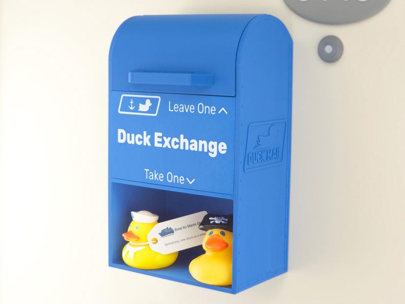May include: A blue Duck Exchange box with the words "Duck Exchange" and "Leave One" and "Take One" printed on the front. Two yellow rubber ducks are inside the box. One duck wears a sailor hat.