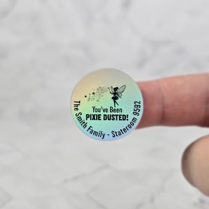Puede incluir: Una pegatina redonda iridiscente con un dise&ntilde;o de hada. La pegatina dice "You've Been Pixie Dusted!" y "The Smith Family - Stateroom 9592".