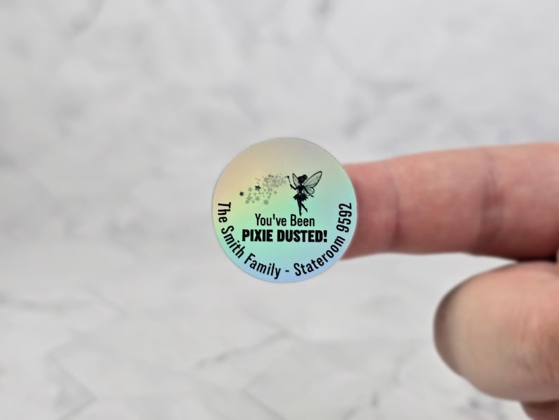 Puede incluir: Una pegatina redonda iridiscente con un dise&ntilde;o de hada. La pegatina dice "You've Been Pixie Dusted!" y "The Smith Family - Stateroom 9592".