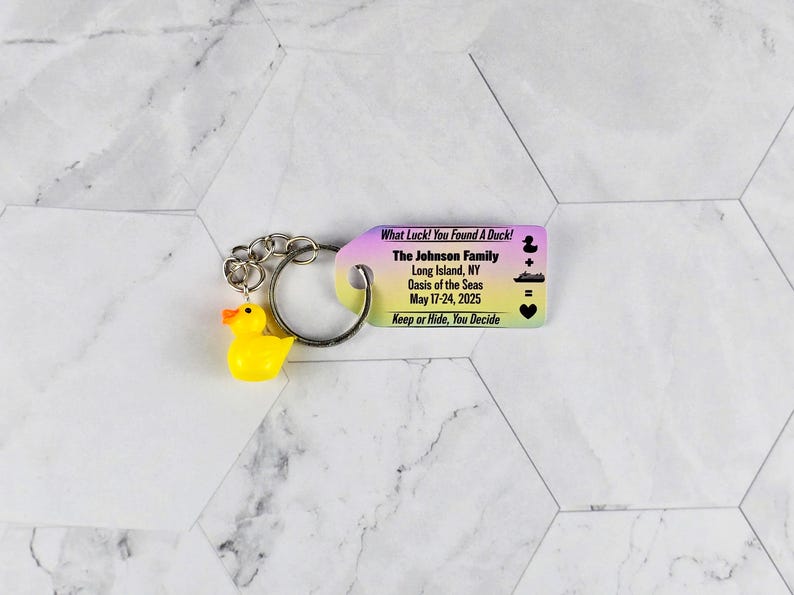 Puede incluir: Un llavero de pato de goma amarillo con una etiqueta de colores arco&iacute;ris que dice "What Luck! You Found A Duck! The Johnson Family Long Island, NY Oasis of the Seas May 17-24, 2025 Keep or Hide, You Decide"