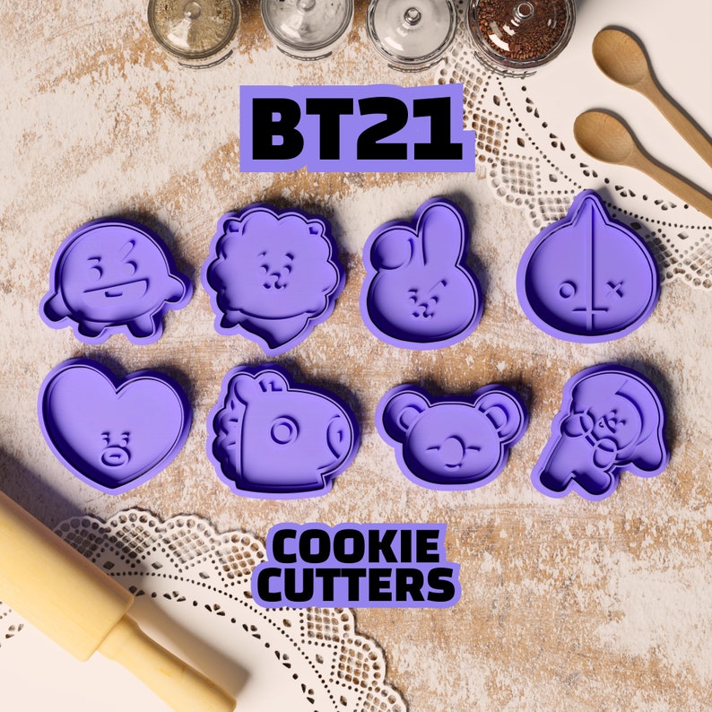 May include: A set of eight purple plastic cookie cutters featuring characters from the BT21 line. The cutters are shaped like a heart, a bear, a bunny, a sheep, a dog, a pig, a round character with an X on it, and a round character with a 3 on it. The text "BT21" and "COOKIE CUTTERS" is printed in black on a white background.