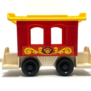 May include: A vintage toy train car with a red body, yellow roof, and cream-colored undercarriage. The car features two black wheels, two windows, and a decorative sticker with a monkey face. Made in the USA.