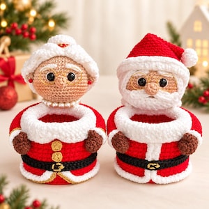 May include: Two crochet baskets shaped like Santa Claus and Mrs. Claus. Both feature red and white yarn, black belts with gold buckles, and white fuzzy trim. Mrs. Claus wears a white bun and pearl necklace, while Santa has a white beard and red hat.
